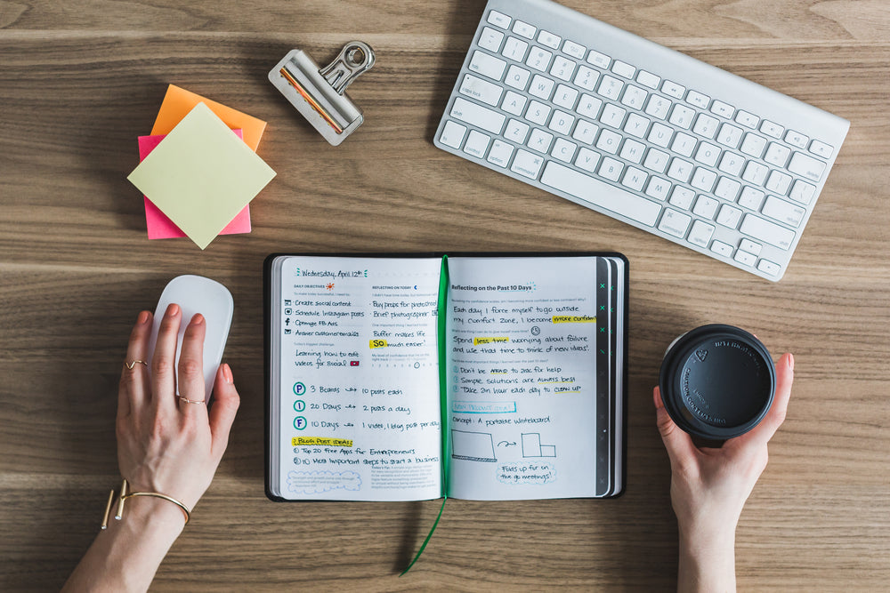 An open journal, coffee and keyboard on a wooden desk